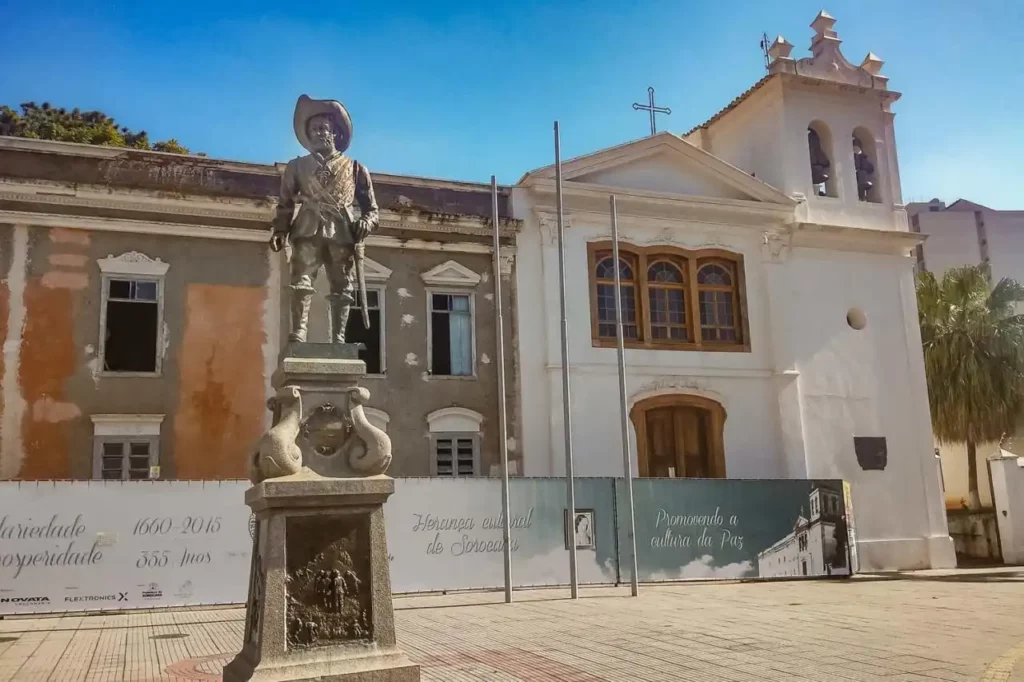 Imagem de uma praça em Sorocaba com uma estátua de um cavaleiro em destaque, ao lado de uma igreja antiga de arquitetura colonial, ideal para quem busca morar ou investir na cidade.